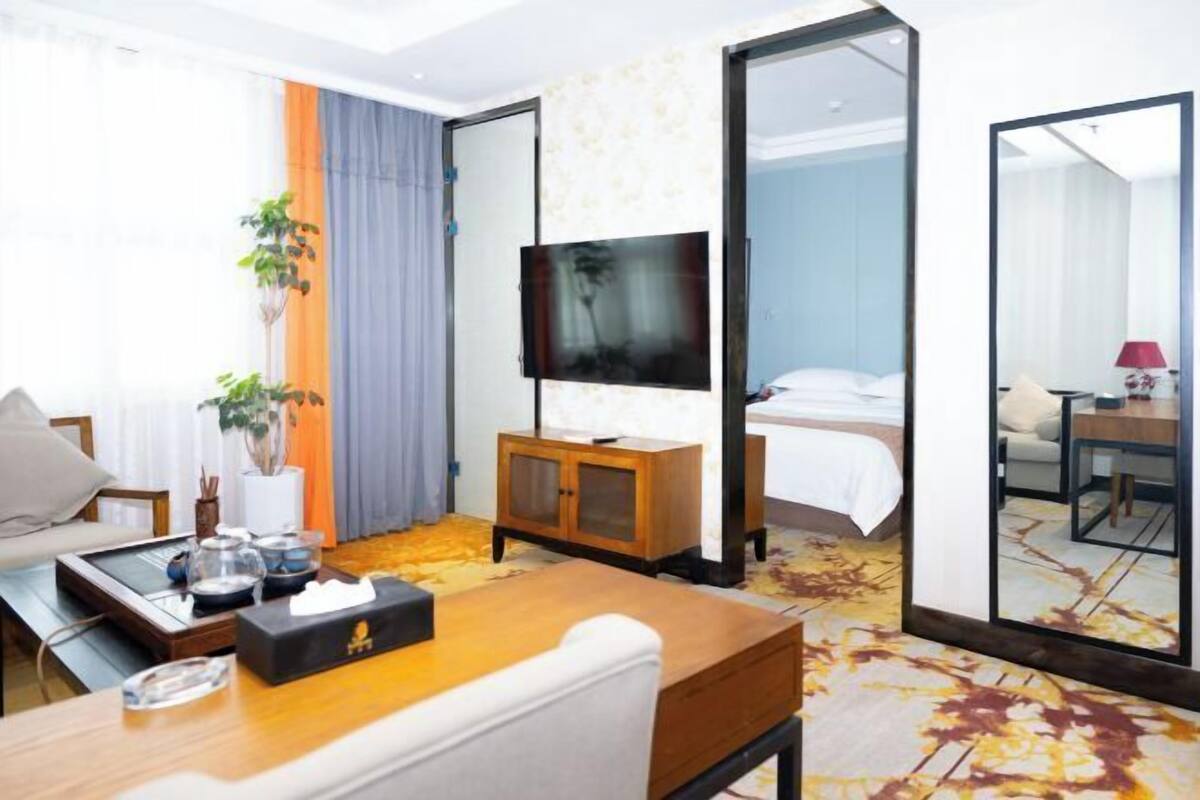 A hotel room with a bed, a TV, a desk with a chair, a coffee table, and a large mirror.