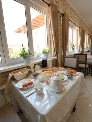 A breakfast table set with various dishes, a window with curtains, and a view of the outside.