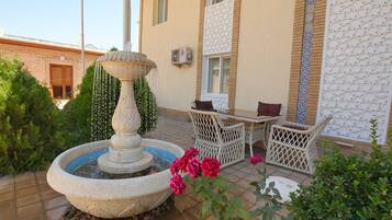A courtyard with a stone fountain, outdoor seating, and a building with patterned walls.