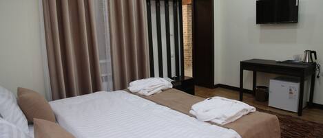 A hotel room with two beds, a desk, a television, and a small refrigerator.