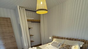 Ein ordentlich bezogenes Bett mit weißen Laken und einer grünen Tagesdecke, eine Pendelleuchte und ein Holzkopfteil.