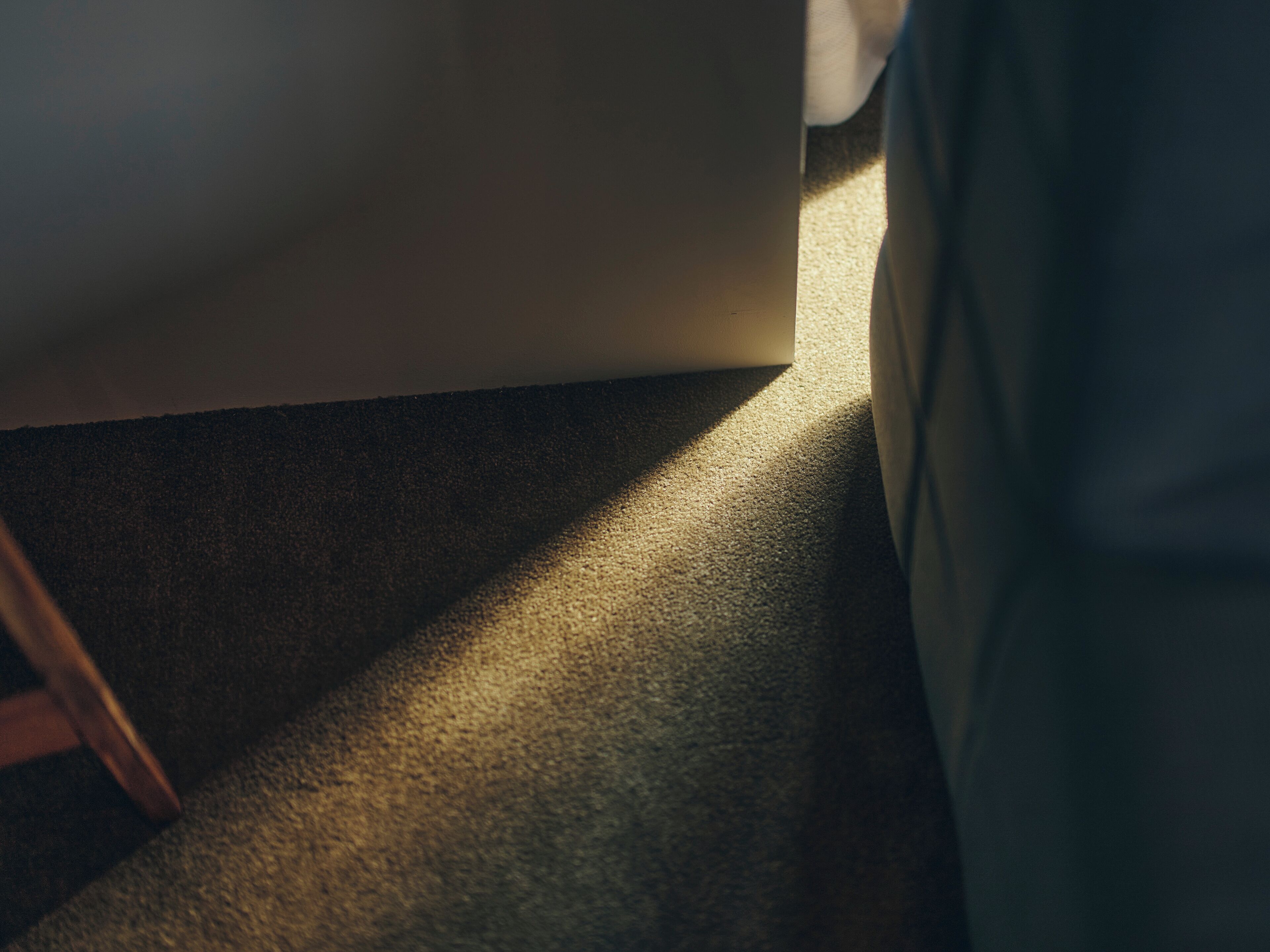 A carpeted floor with a shadow cast by a piece of furniture.