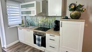 A modern kitchen with white cabinets, a black stove, and a tiled backsplash. - Gästehaus am Ruppiner See (Neuruppin)