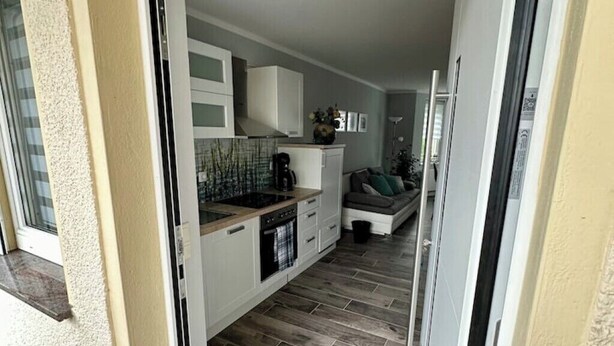 A compact kitchen with modern appliances, a dining area with a sofa, and a view of the outside. - Gästehaus am Ruppiner See (Neuruppin)