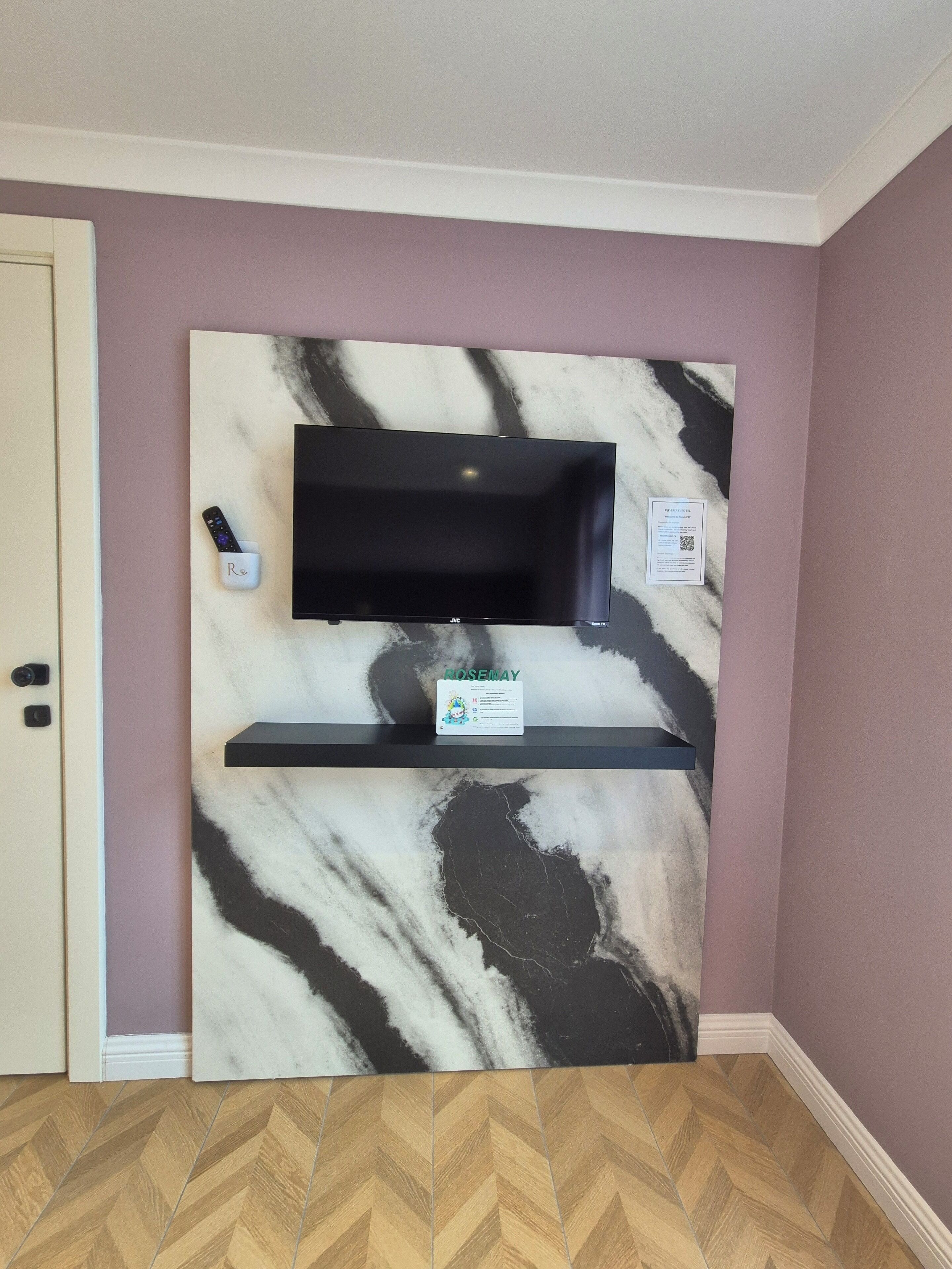 A room with a marble wall, a mounted TV, a remote control holder, and a sign.