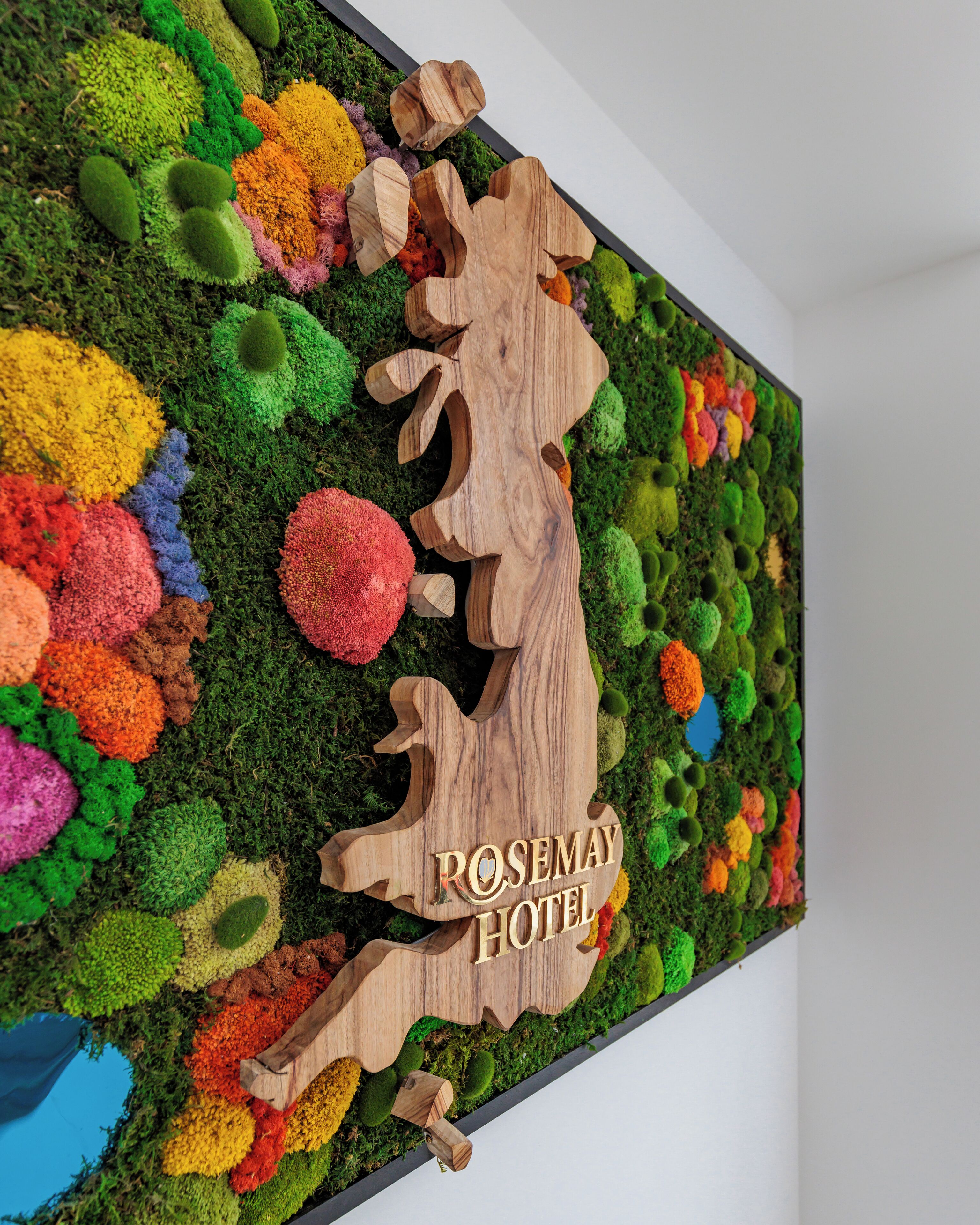 A wall-mounted sign with the text "ROSEMARY HOTEL" surrounded by colorful moss-like decorations.