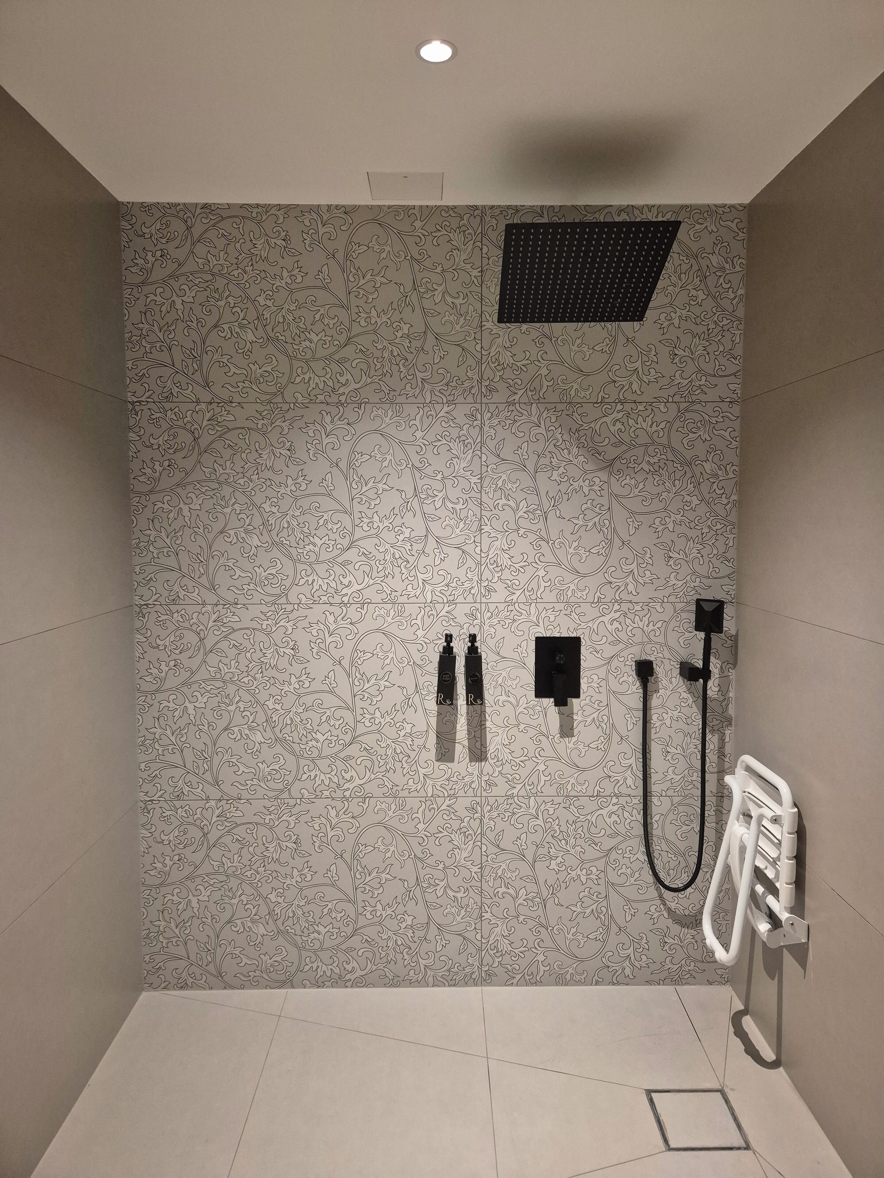 Uma área de chuveiro com parede estampada, uma luminária no teto e um radiador branco.