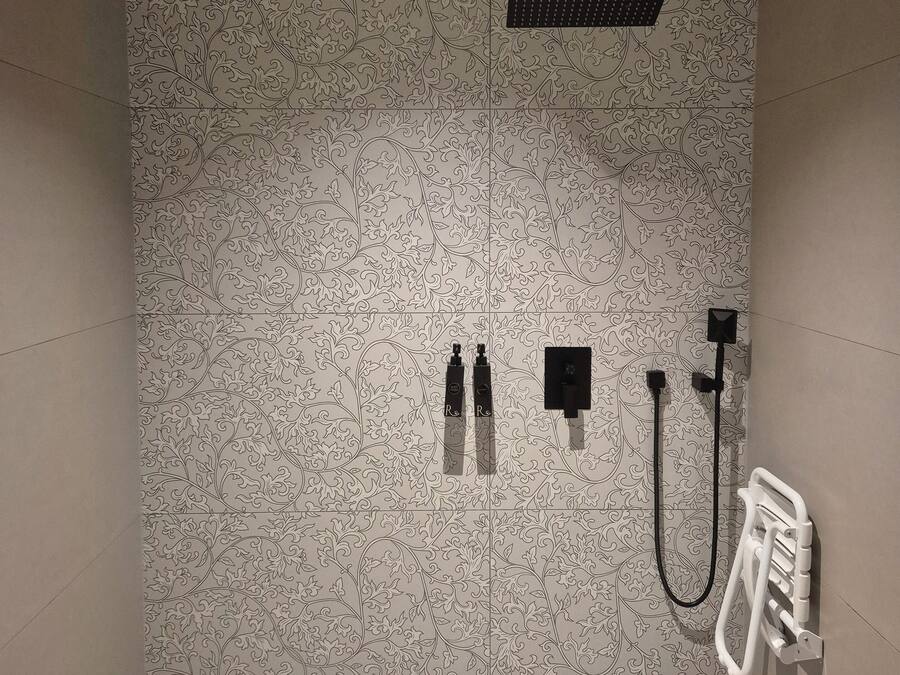 Uma área de chuveiro com parede estampada, uma luminária no teto e um radiador branco.