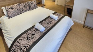 Un dormitorio moderno con cabecera de madera, una cama grande con ropa de cama estampada, una mesita de noche y vistas a un pasillo que lleva a una escalera.