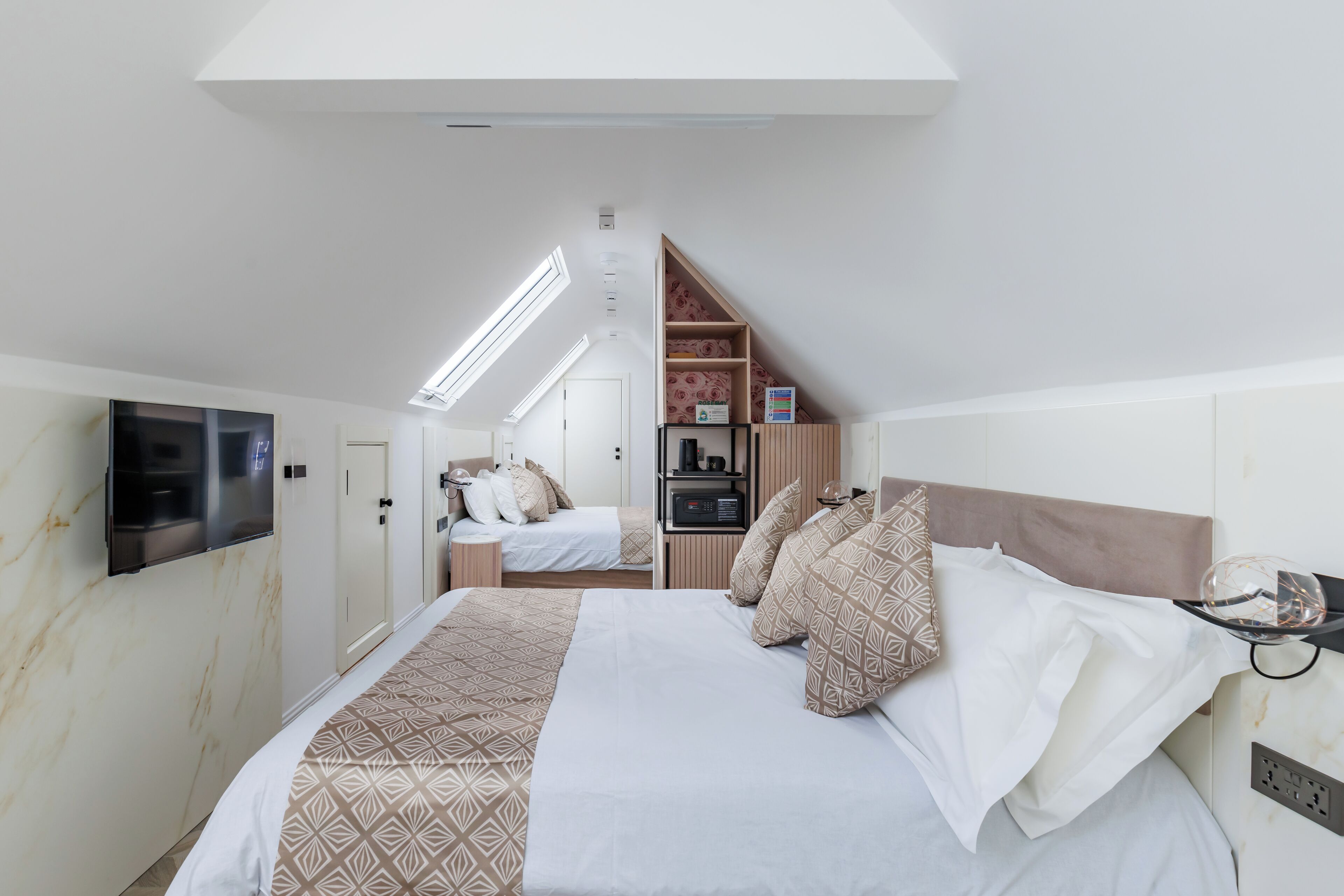 A bedroom with a large bed, a TV mounted on the wall, and a skylight above.