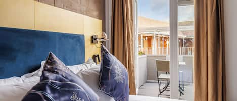 Una habitación de hotel con cama, cabecera, ventana con cortinas y vistas a un espacio exterior.