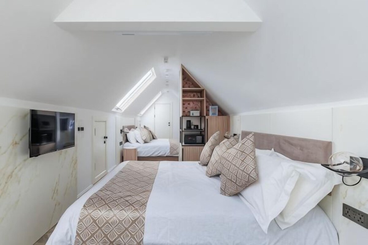 A bedroom with a bed, a TV, a kitchenette, and a staircase.