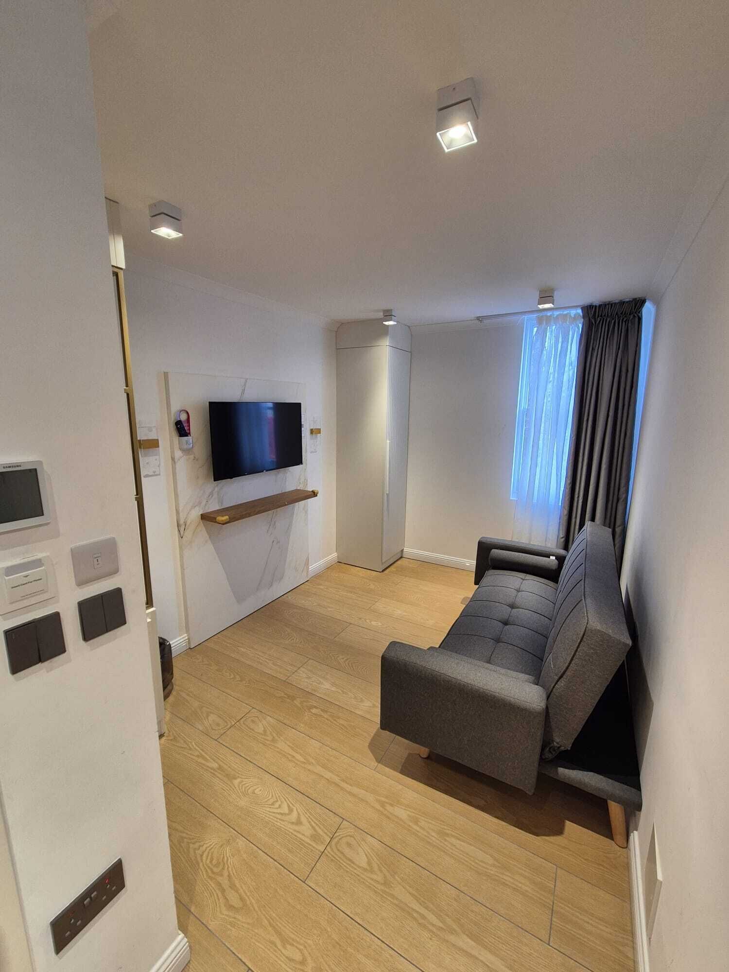 A modern living room with a flat-screen TV, a sofa, a wooden floor, and a window with curtains.