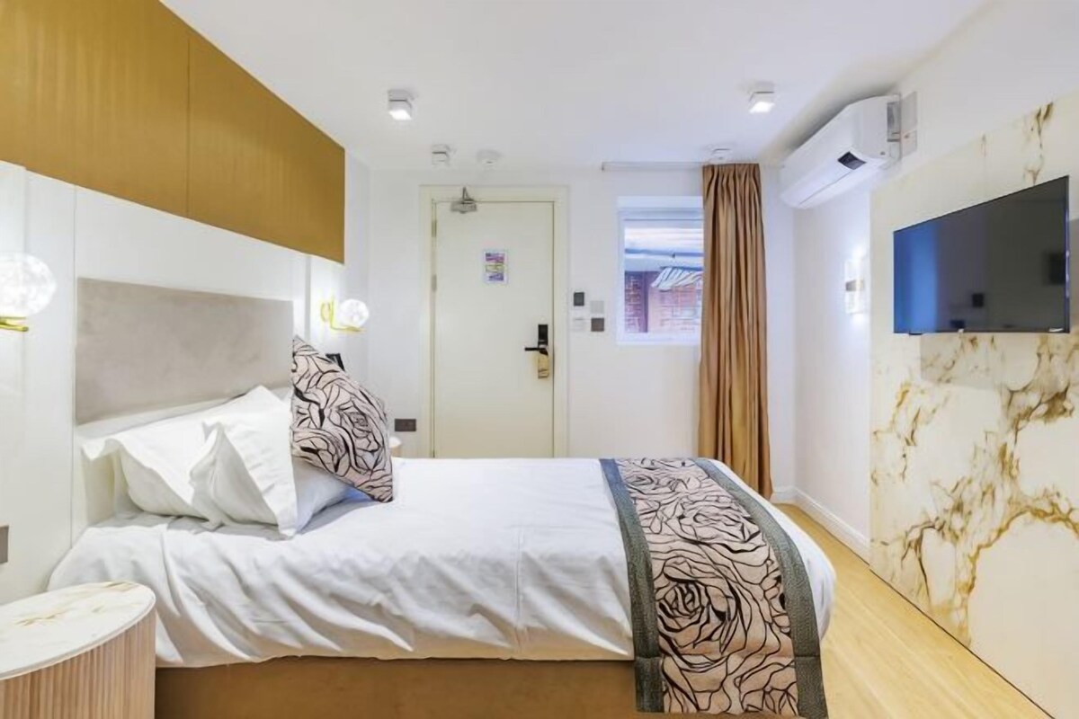 Habitación de hotel con cama, mesita de noche, televisor y pared de mármol.