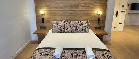 Una habitación de hotel moderna con techo de madera, una cama grande con cubrecama estampado, dos lámparas fijadas a la pared y un televisor en la pared.