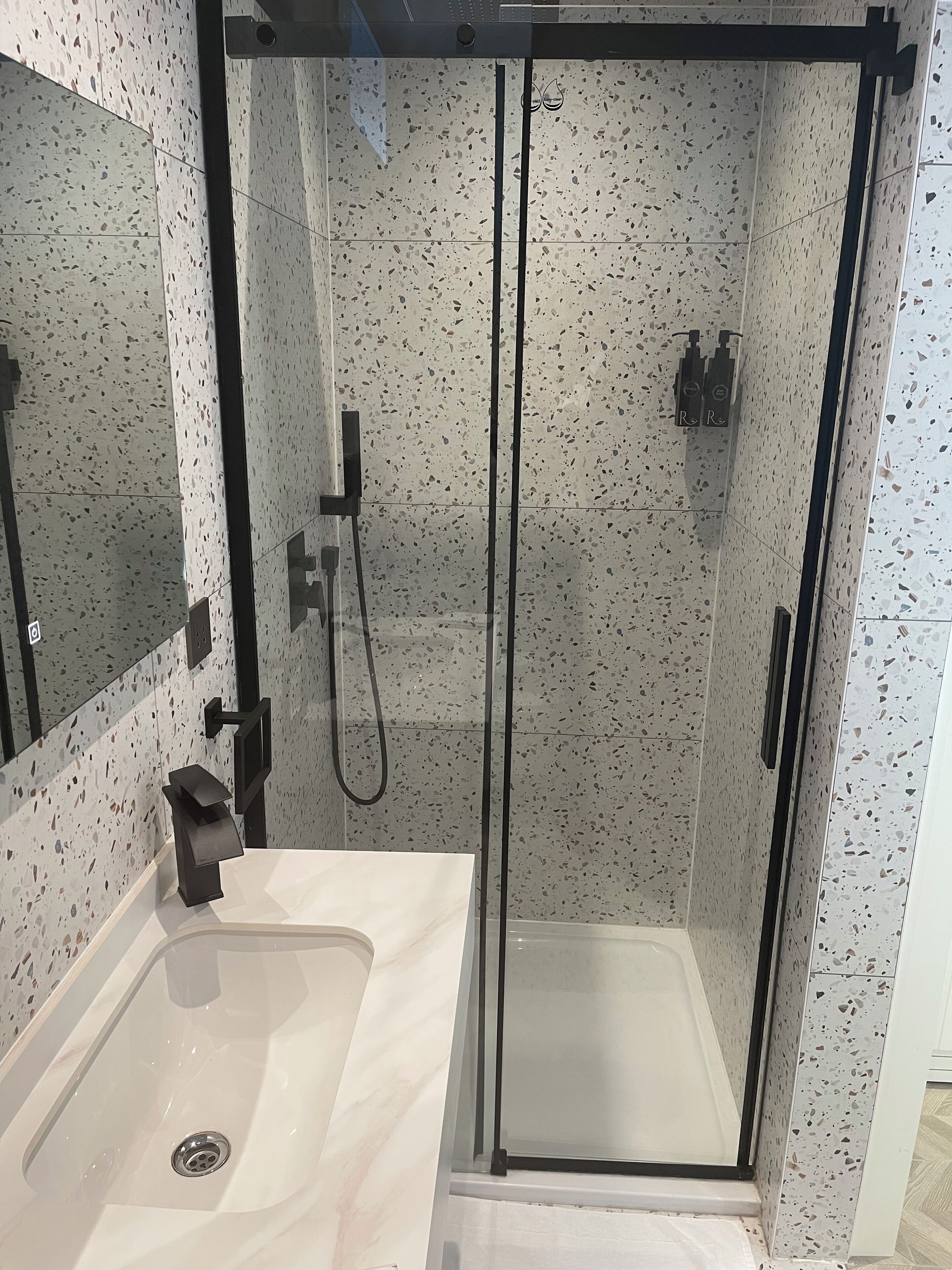A modern bathroom with a glass-enclosed shower, a white sink, and a mirror.