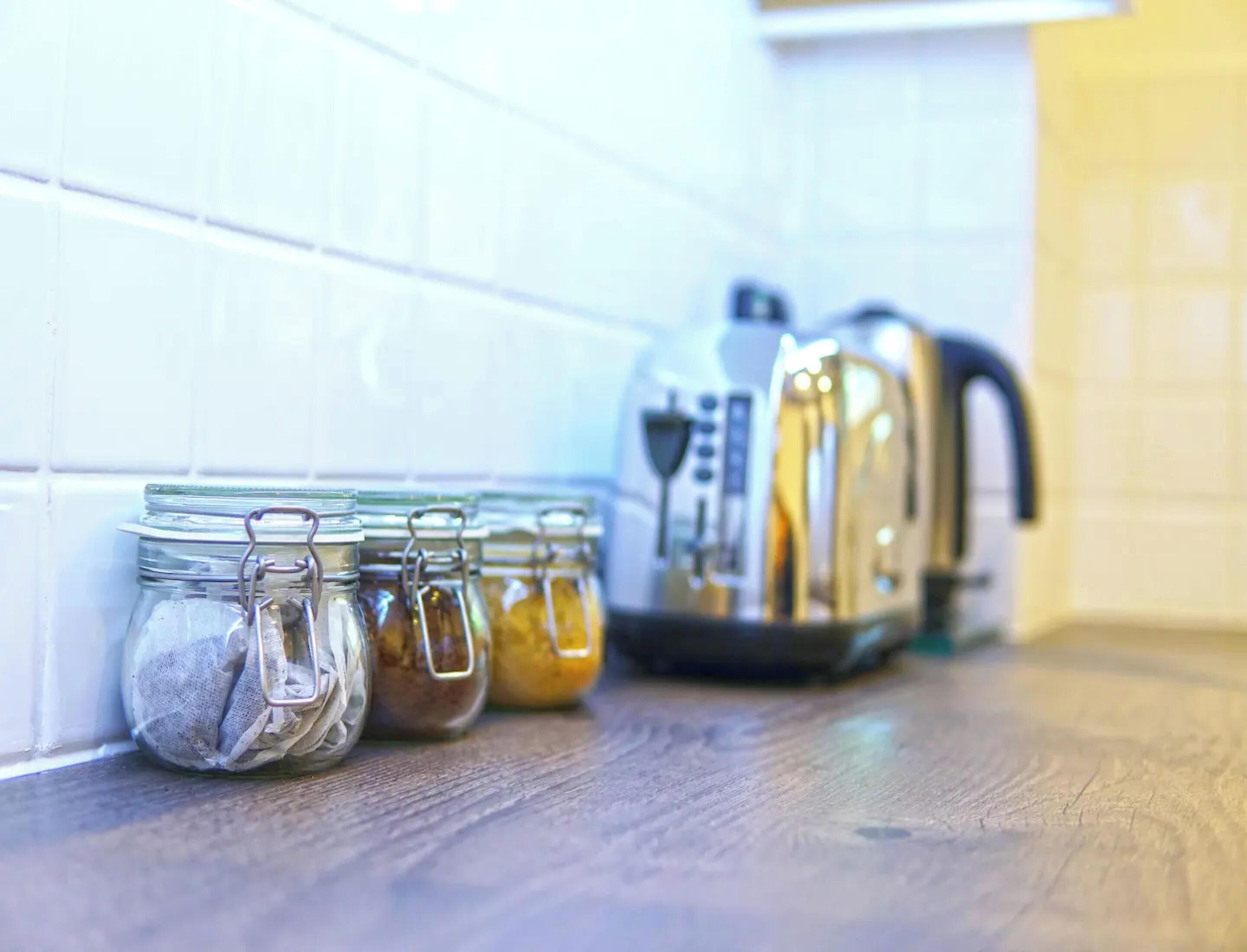A kitchen counter with four glass jars containing different food items and a kettle.