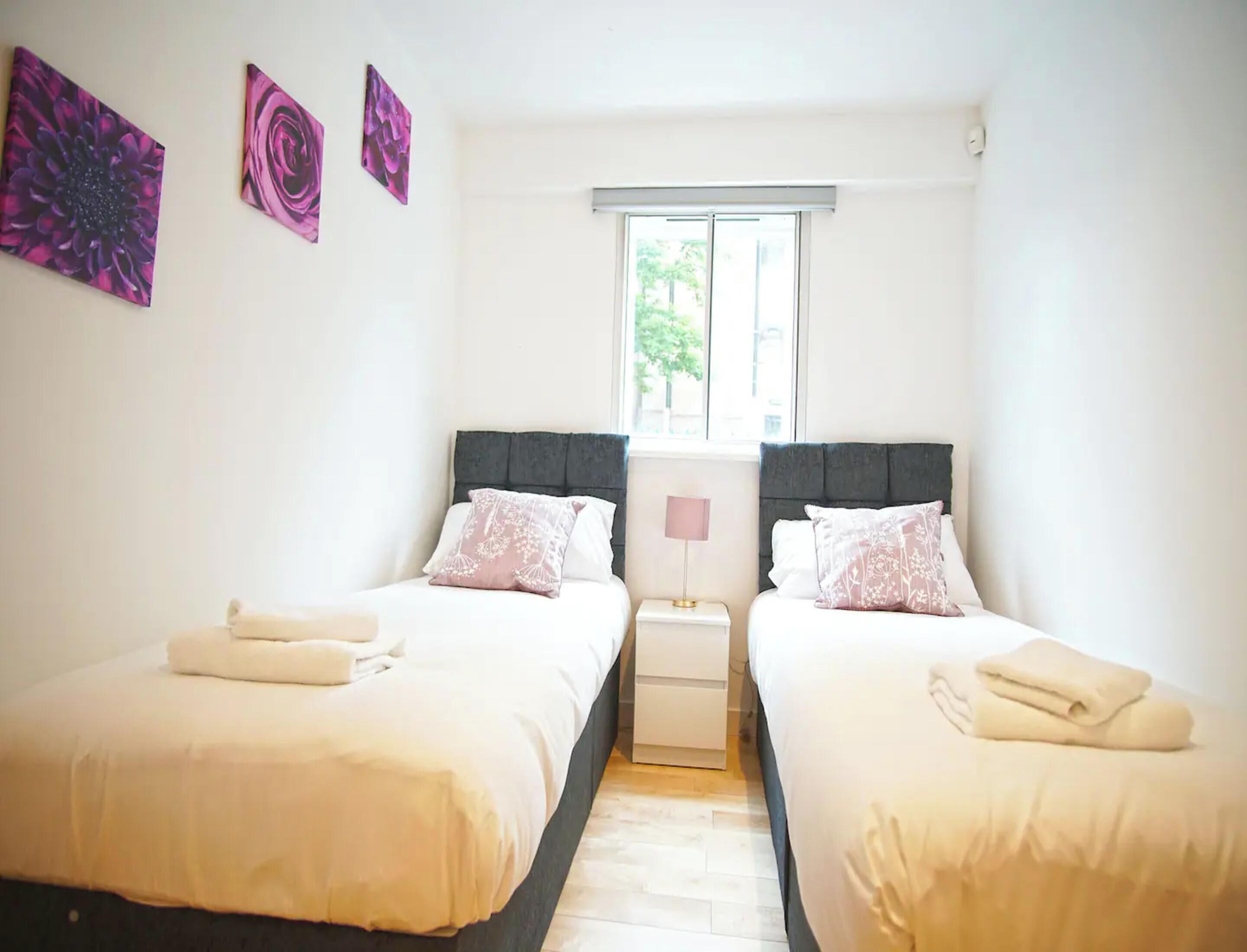 A bedroom with two beds, a window, and artwork on the wall.