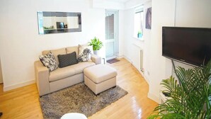 A modern living room with a beige sofa, a flat-screen TV, and a large mirror on the wall. - Superior Canary Wharf  O2 Arena 2Bed (London)