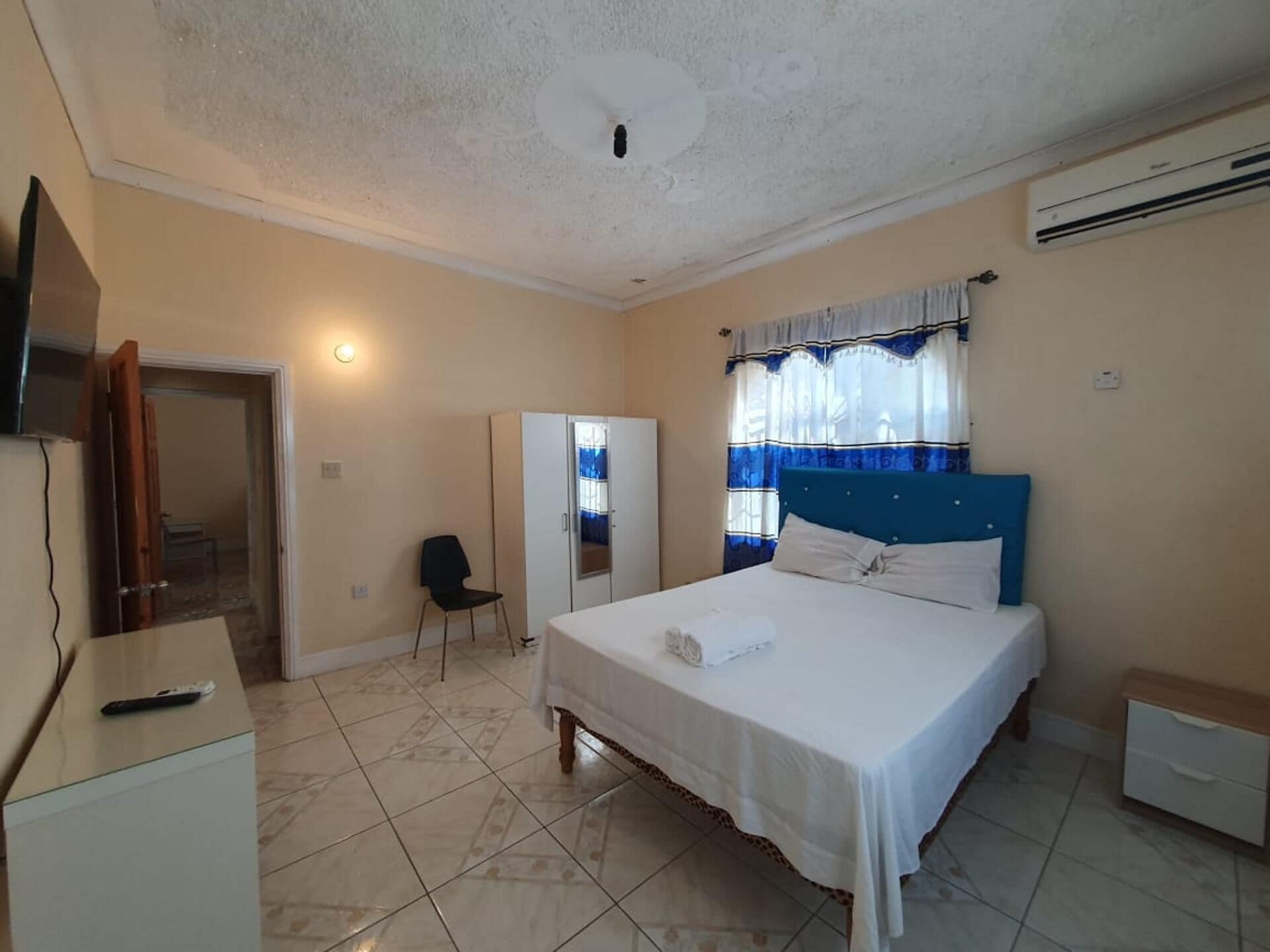 Een slaapkamer met een bed, een bureau, een stoel, een kledingkast en een airconditioning.
