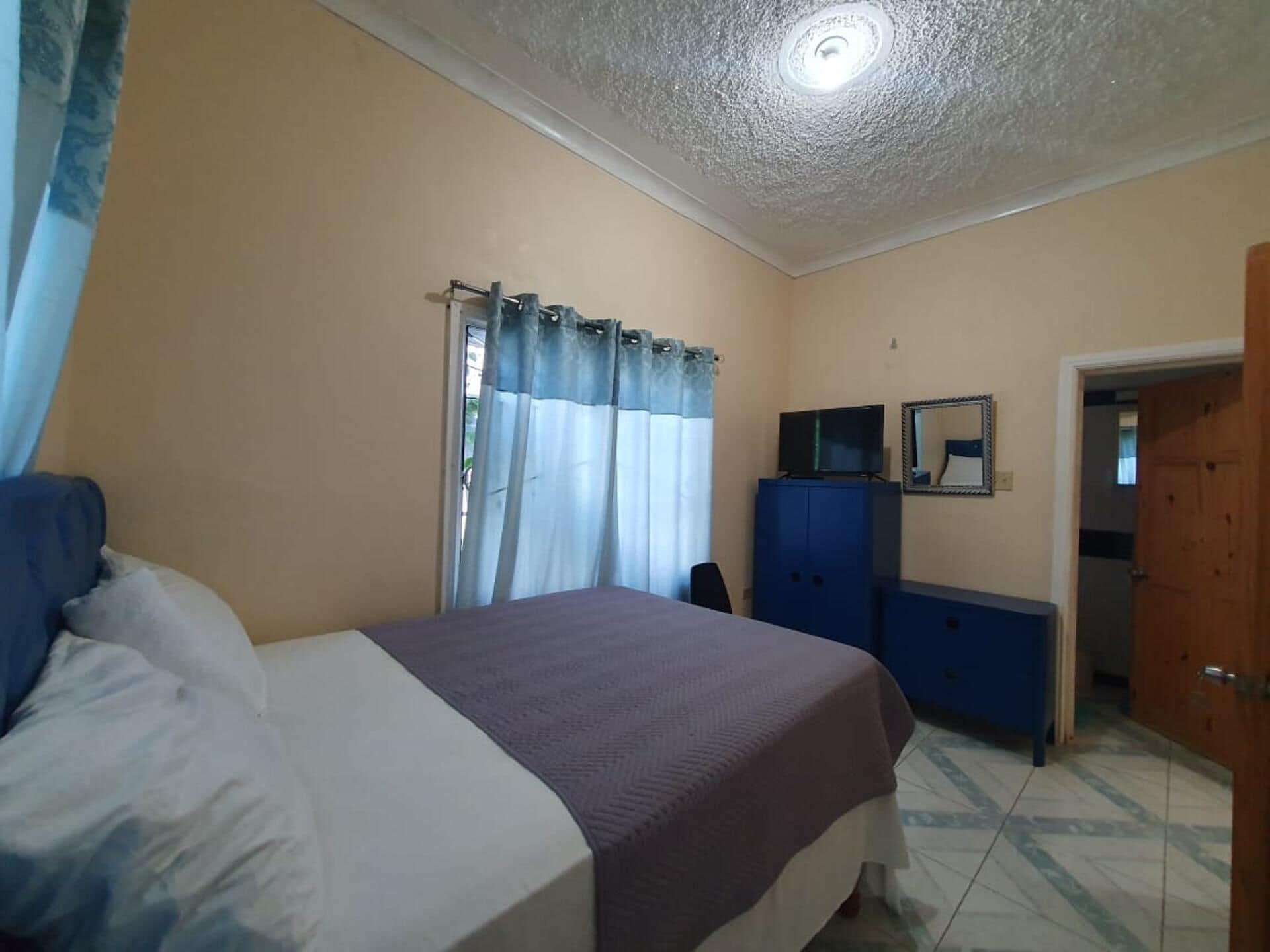 Un dormitorio con cama, cómoda, televisor y puerta.