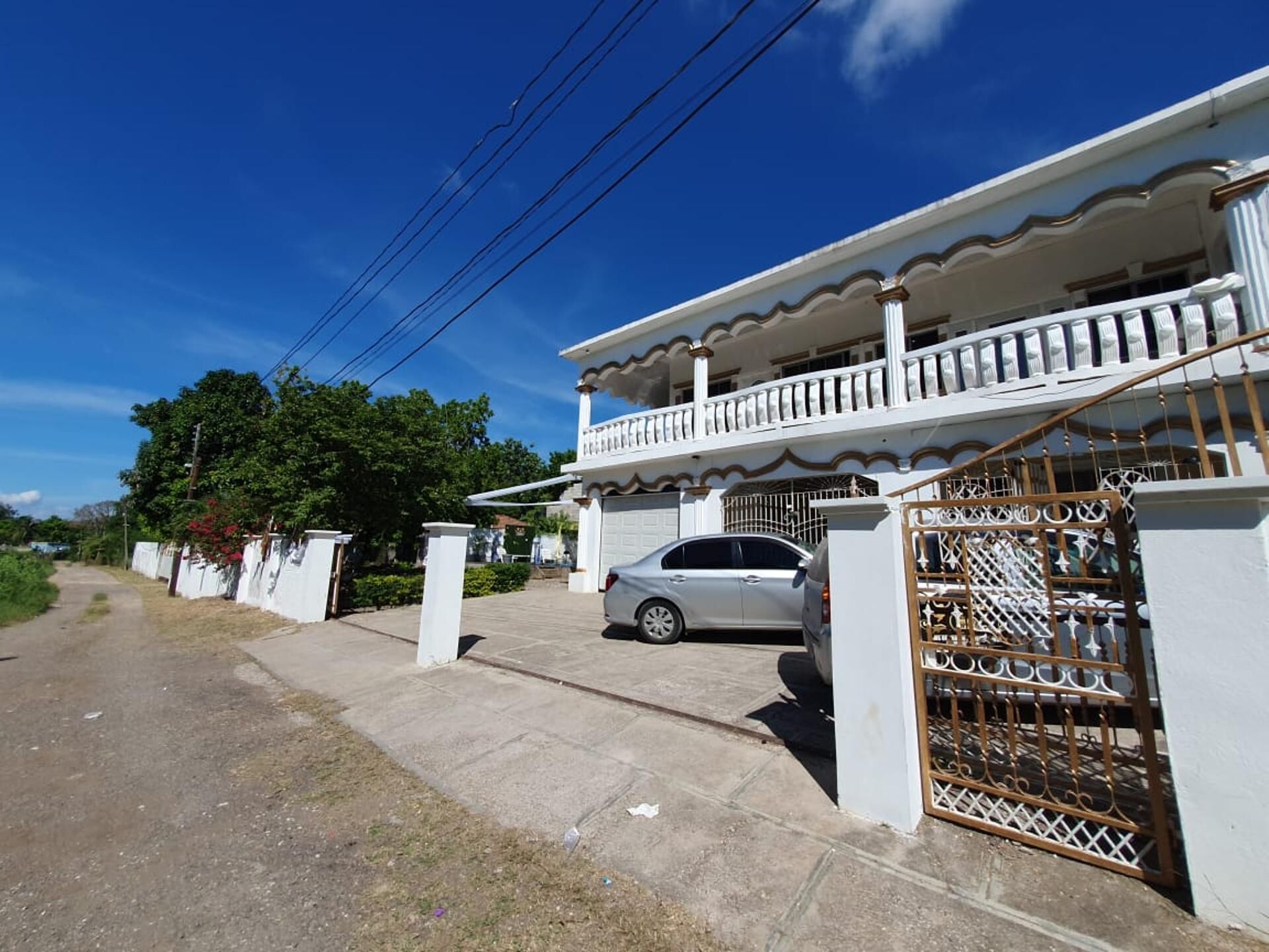 A two-story house with a balcony, a gated entrance, and a parked car.