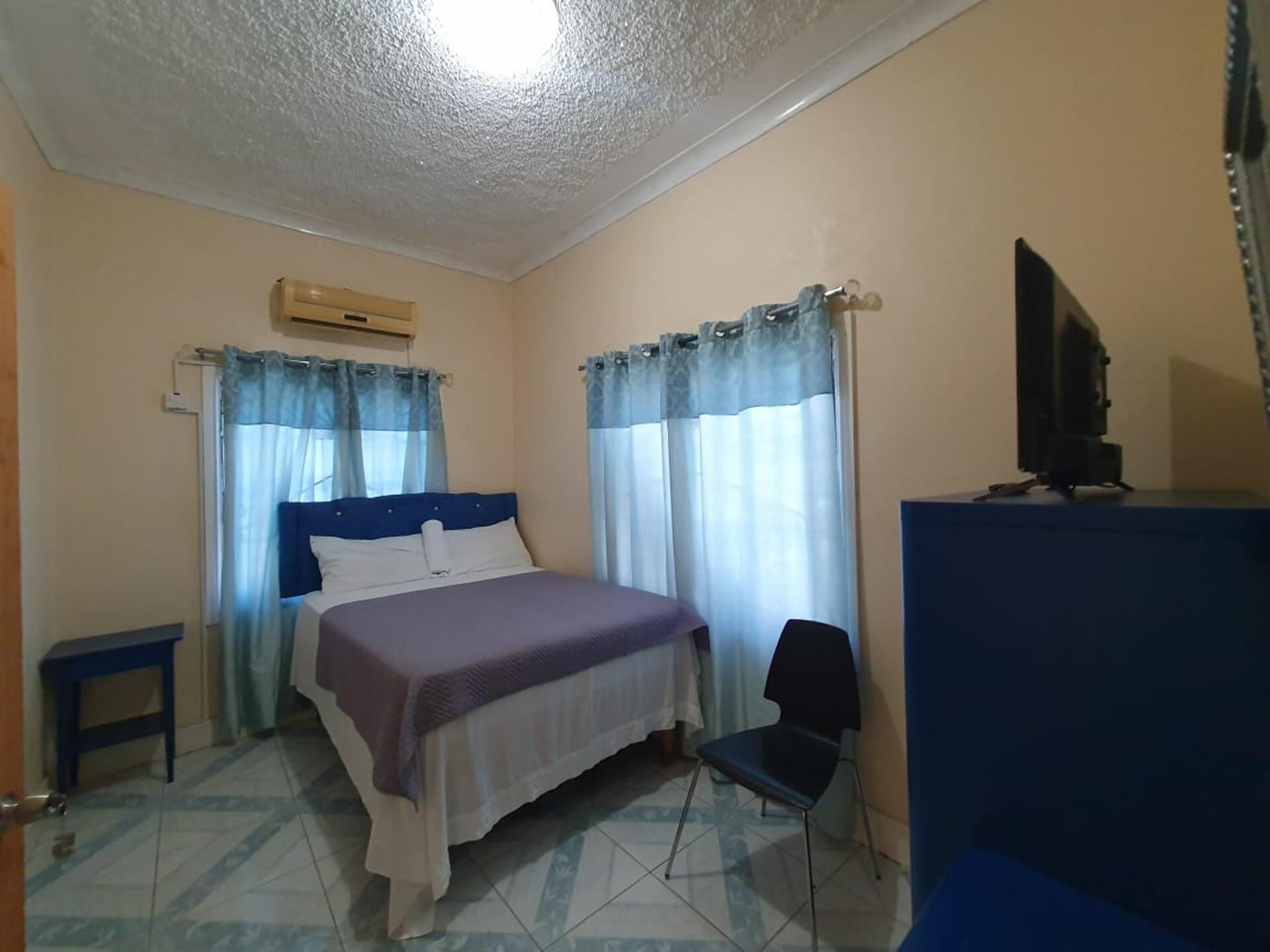 Ein Schlafzimmer mit einem Bett, einem Sessel, einem Fernseher und Vorhängen.