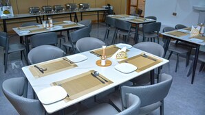 A dining area with tables set for four, each with place settings, chairs, and a buffet line in the background. - UNIQUE ROYAL HOTEL AND SUITES (Dodoma)