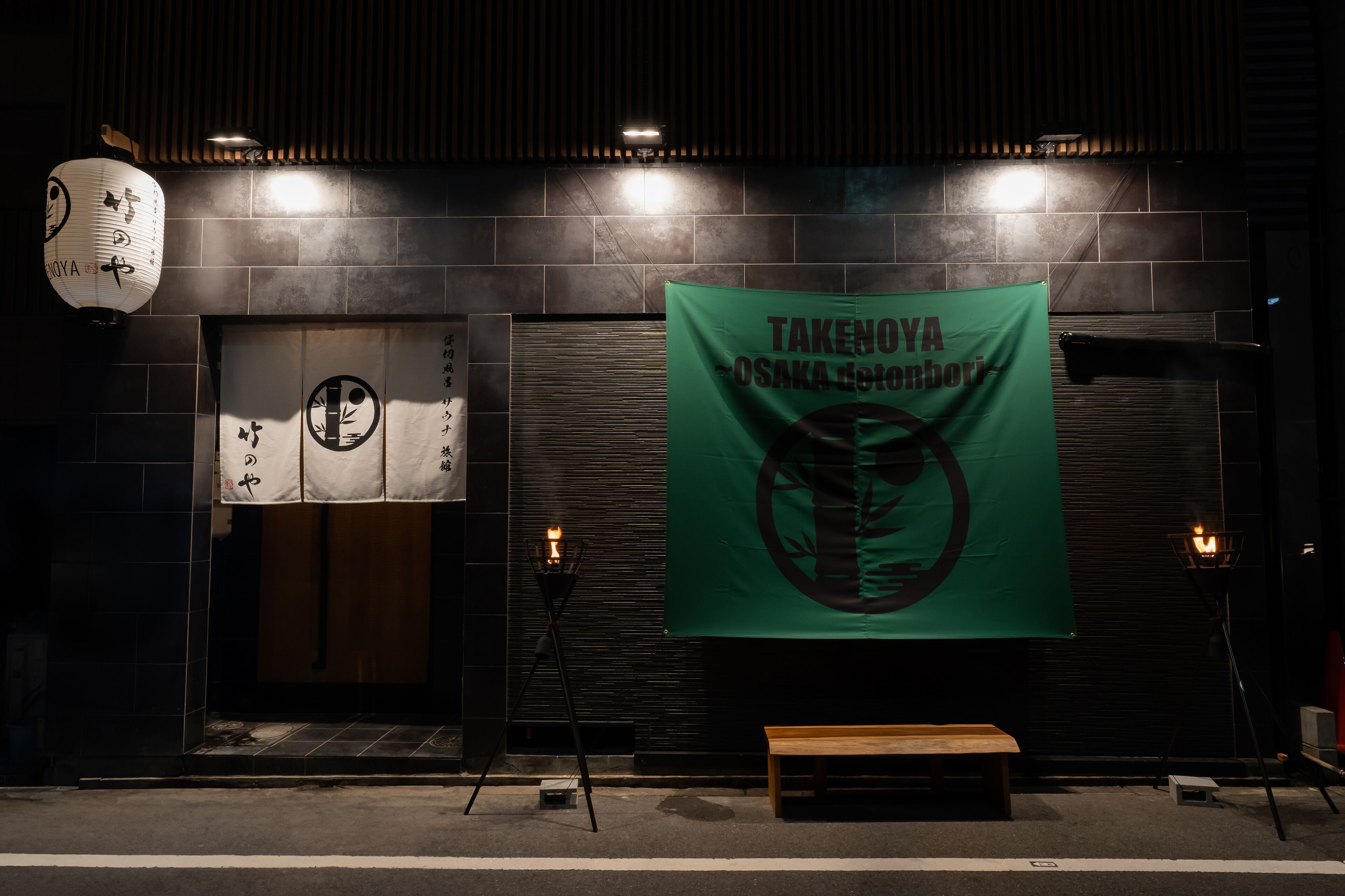 A restaurant entrance with a green banner, a lantern, and a bench outside.