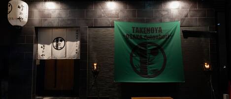 A restaurant entrance with a green banner, a lantern, and a bench outside.