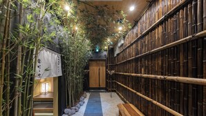 A narrow corridor with bamboo walls, a wooden bench, and a stone pathway. - TAKENOYA (Osaka)