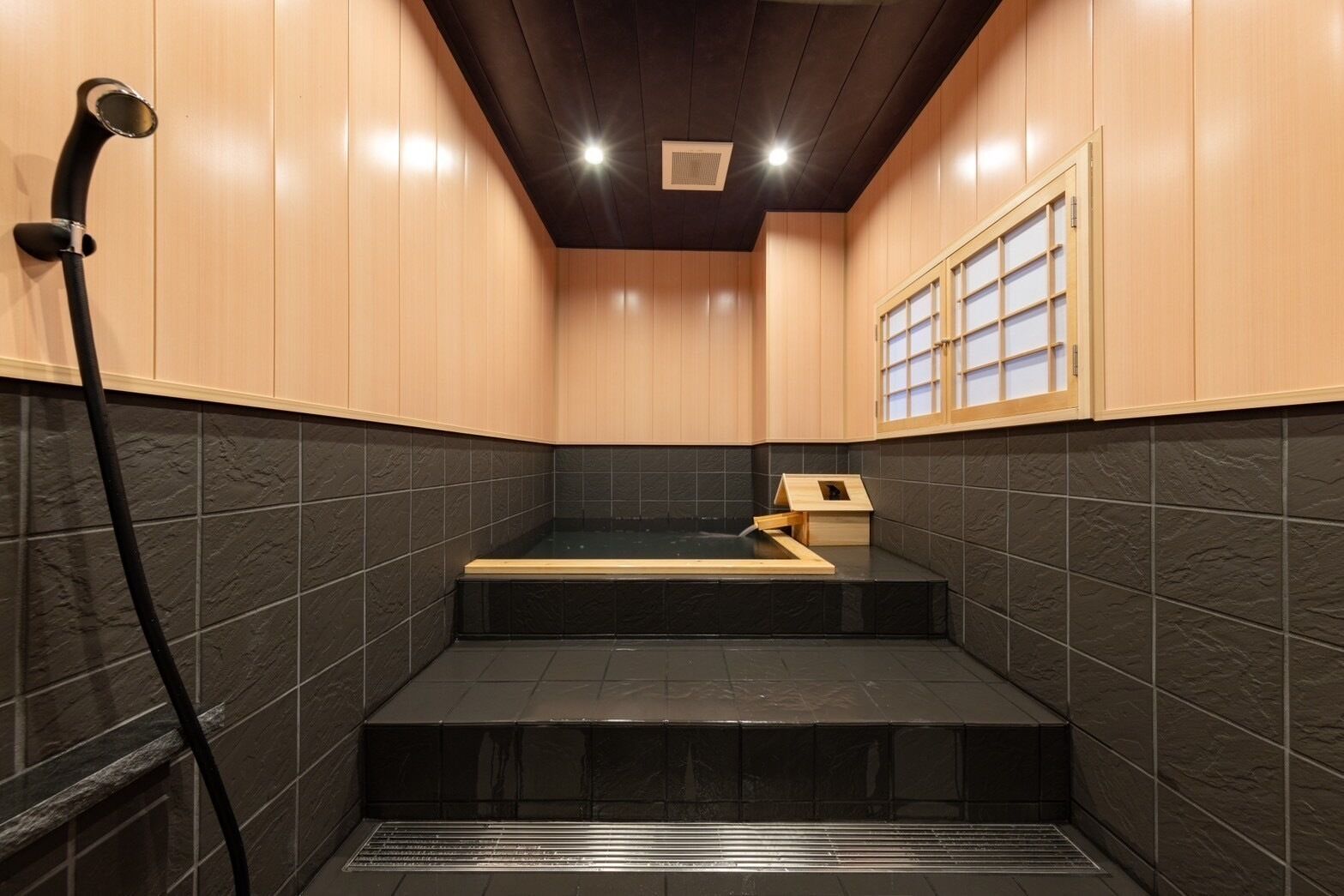A modern bathroom with a black-tiled floor, wooden steps, a wooden cabinet, and a shower area.