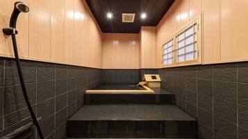 A modern bathroom with a black-tiled floor, wooden steps, a wooden cabinet, and a shower area.