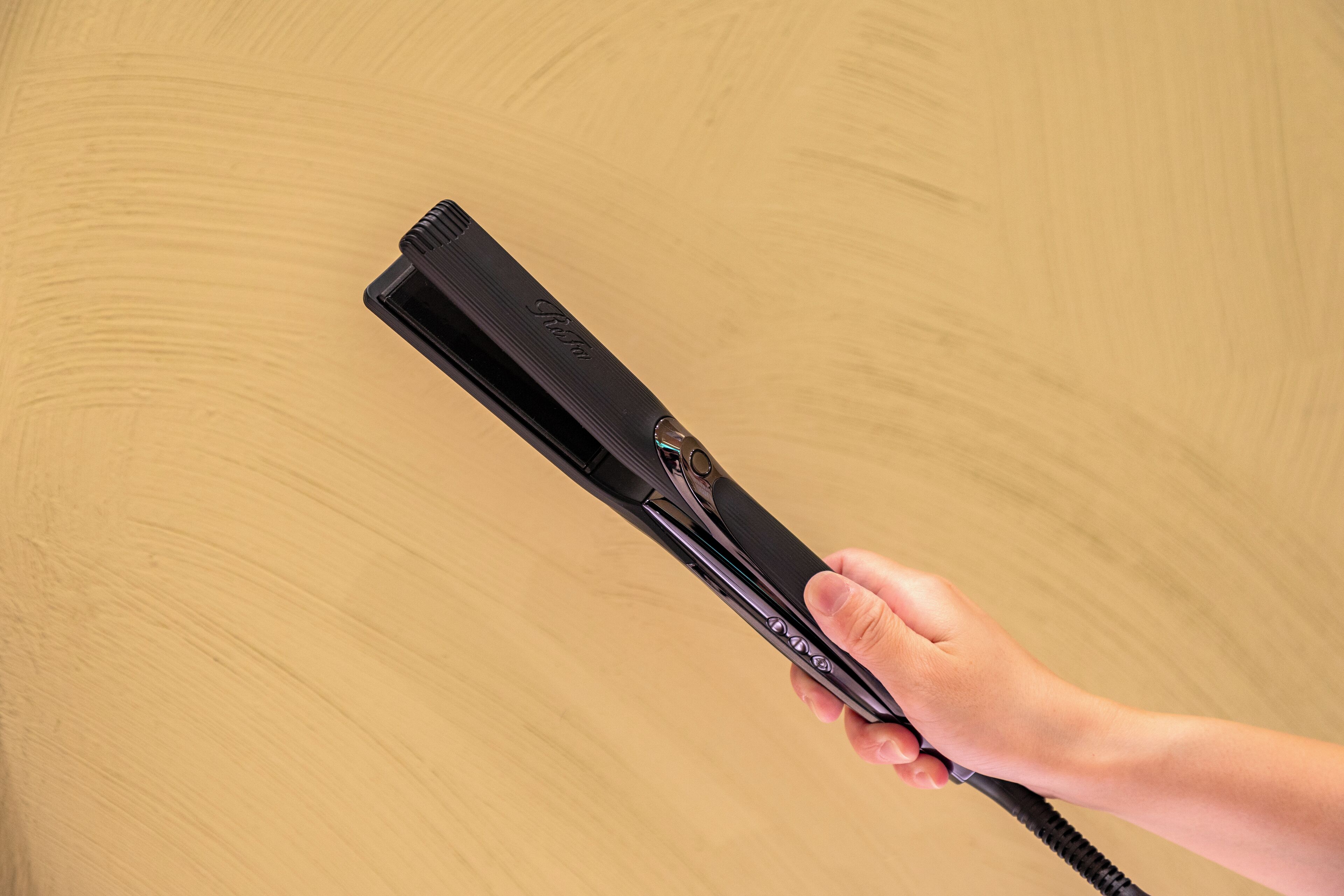 A hand holding a black hair straightener with a cord.