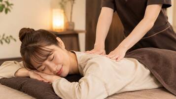 A person receiving a massage in a room with a bed, a small table with a lamp, and a plant.