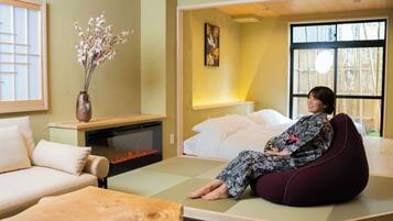 A room with tatami flooring, a low wooden table, a sofa, and a bed with a white headboard.