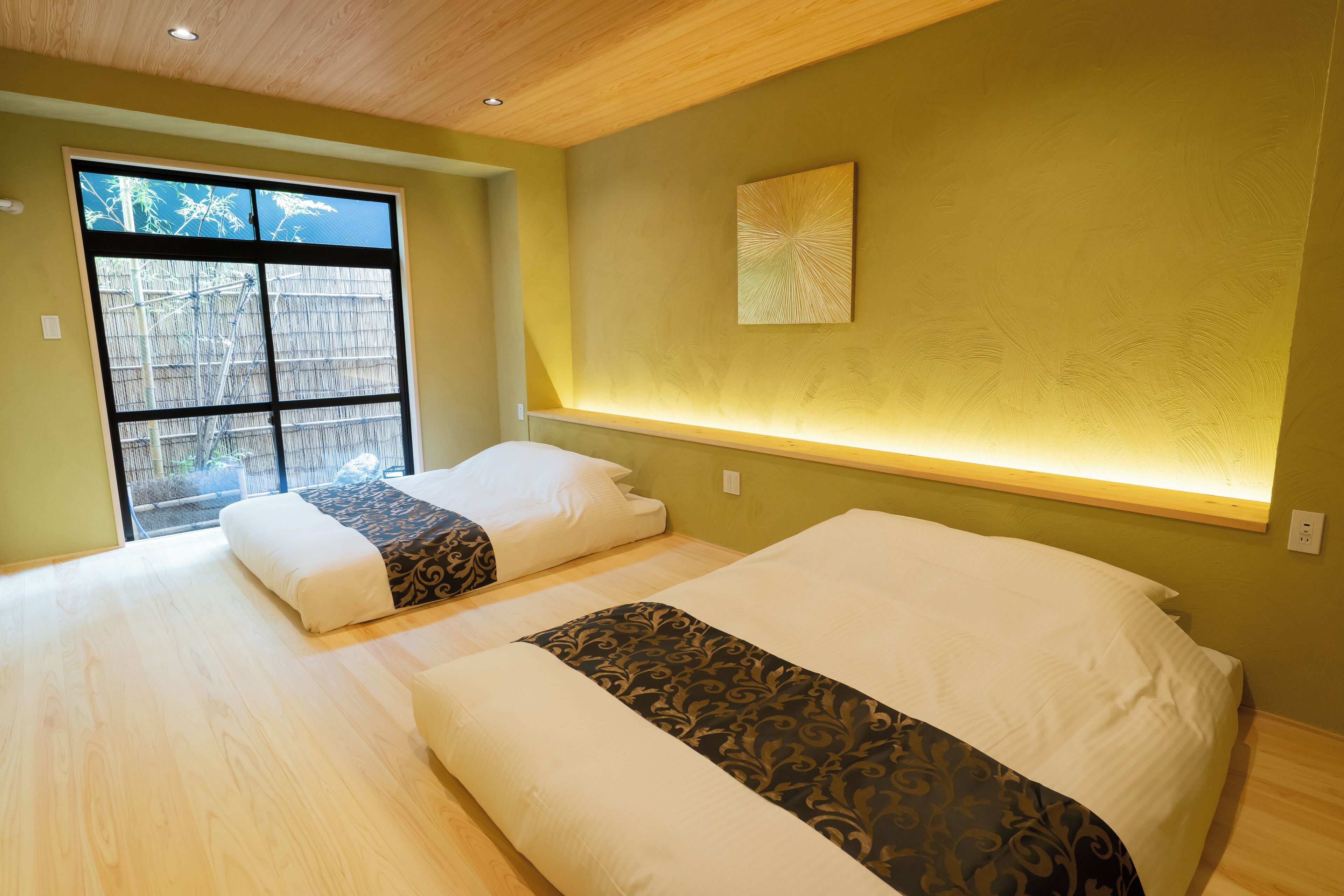 Habitación de hotel con dos camas, un ventanal con vistas a bambú y una lámpara fijada a la pared.