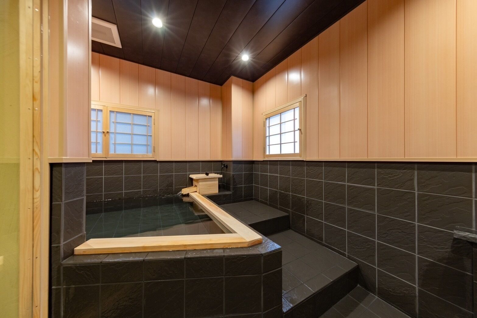 Un baño moderno con pared de azulejos negros, muebles de madera y un banco empotrado de madera.