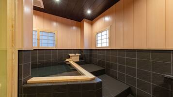 Un baño moderno con pared de azulejos negros, muebles de madera y un banco empotrado de madera.