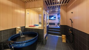 A modern bathroom with a large blue hot tub, a wooden bench, a small wooden stool, and a shower area. - TAKENOYA (Osaka)
