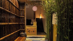 A traditional Japanese interior with a wooden bench, bamboo wall, and a stone pathway leading to a reception area. - TAKENOYA (Osaka)