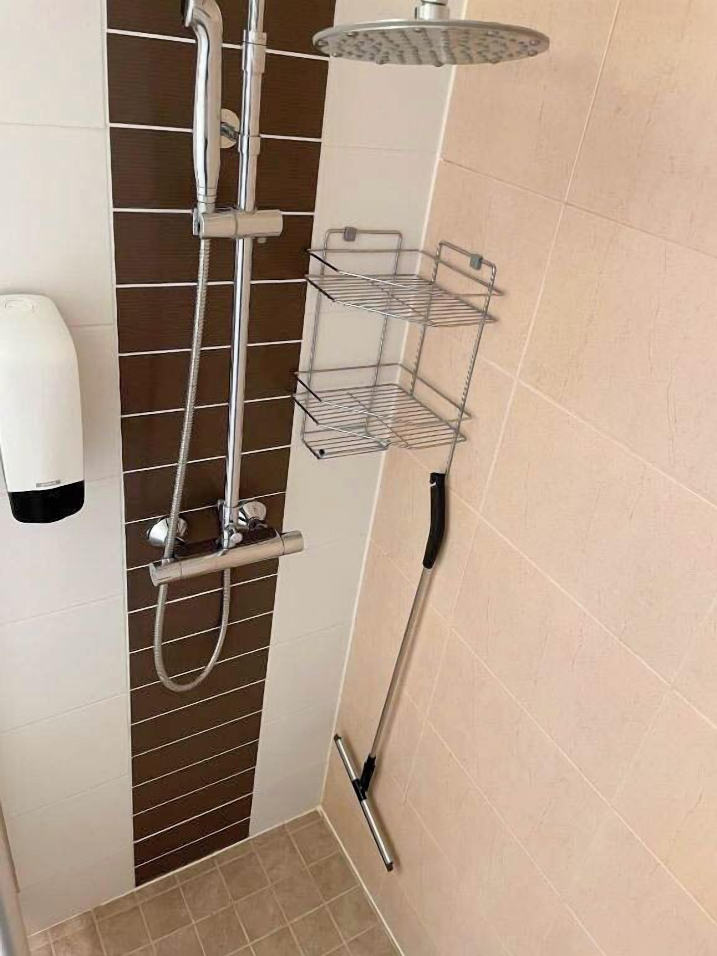 Un espace douche équipé d’un pommeau de douche à main, d’un pommeau de douche fixé au mur et d’un flexible de douche à main. Deux paniers en fil métallique sont fixés au mur.