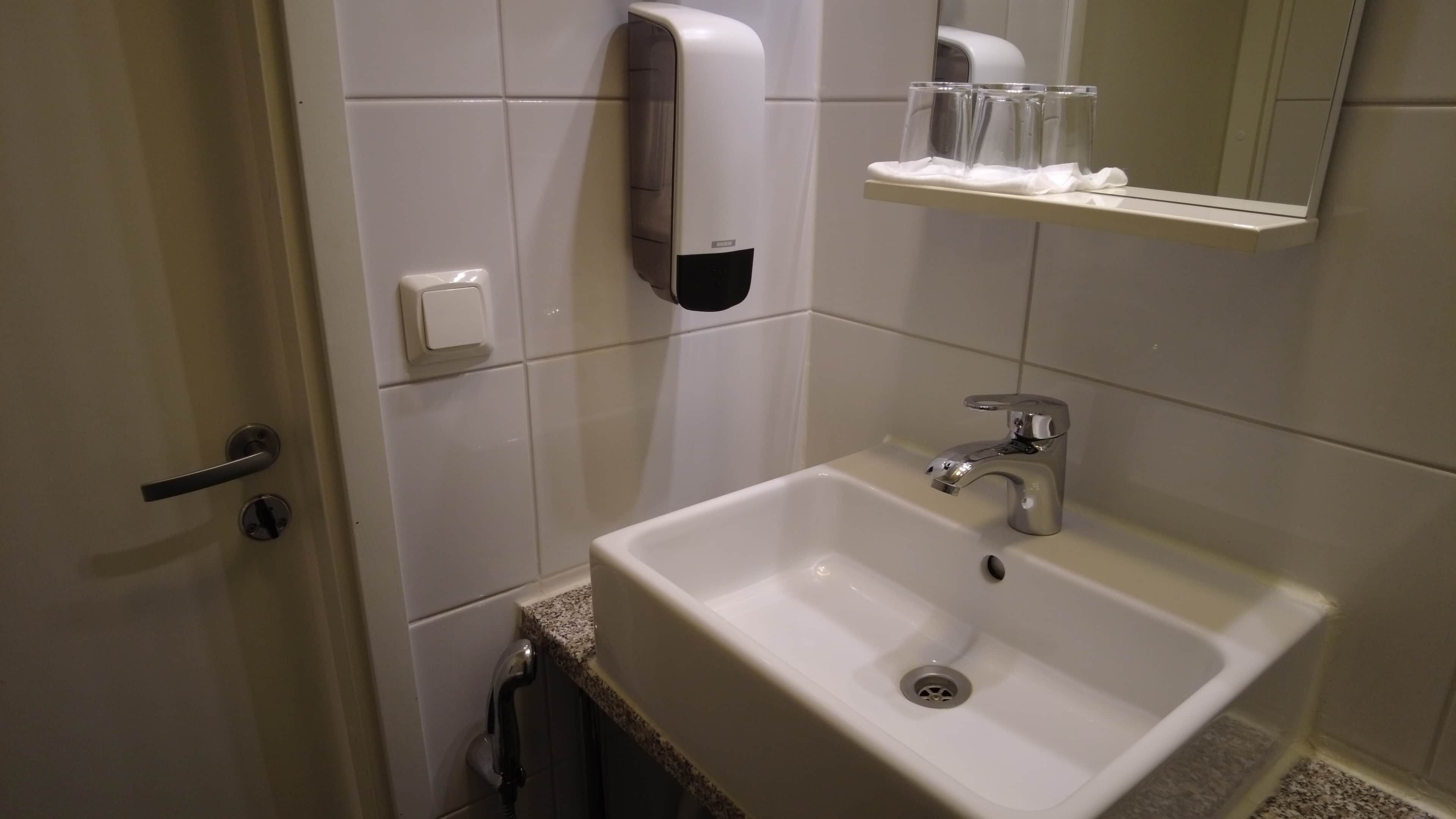 A bathroom with a sink, a hand dryer, a soap dispenser, and a mirror.