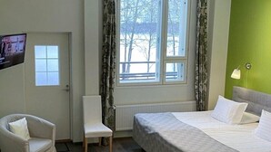 Une chambre d’hôtel avec un lit, une chaise, une petite table, un téléviseur et une fenêtre avec des rideaux.