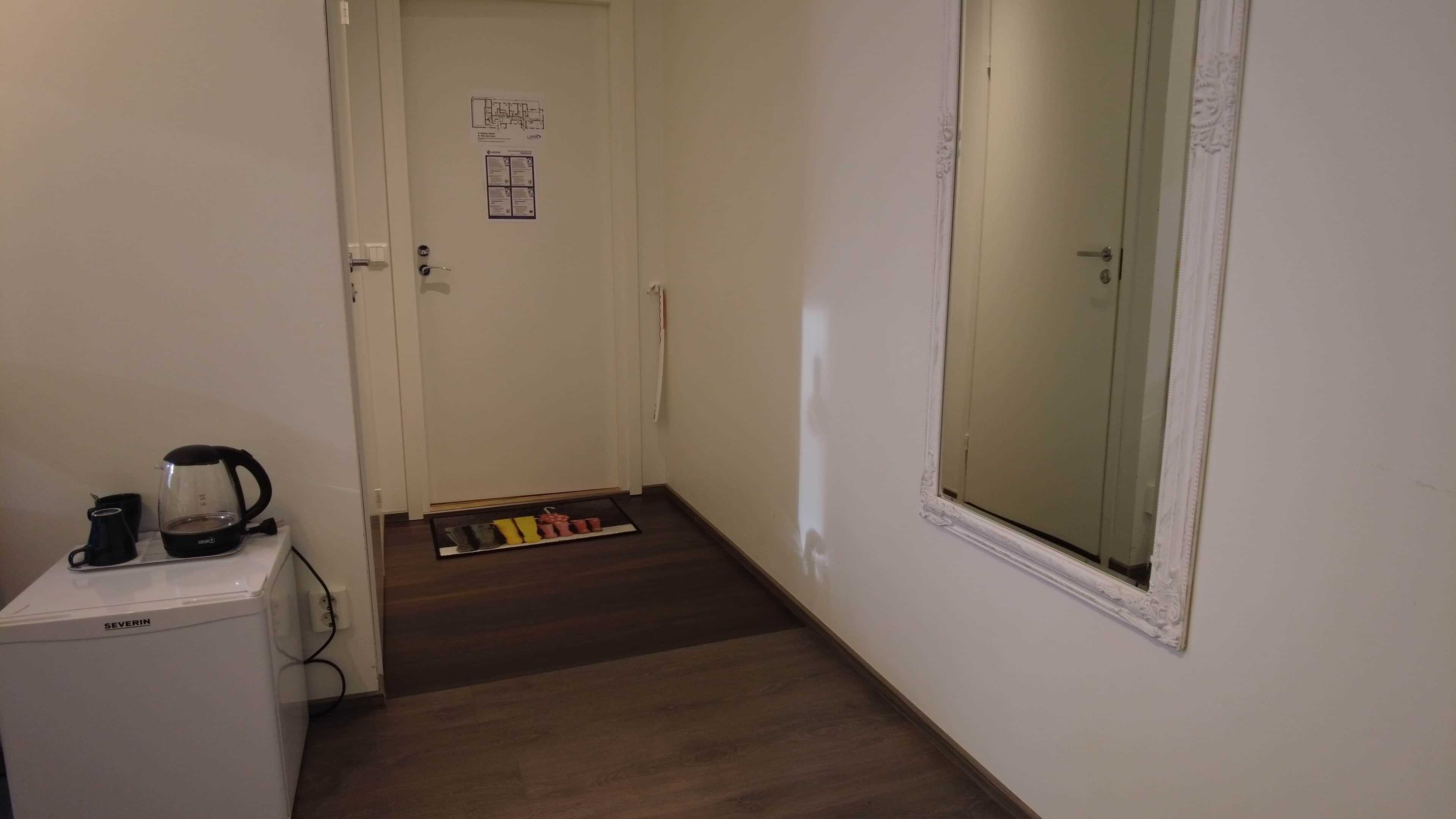 A small kitchenette with a coffee maker and a kettle, a door with a floor plan, and a window with a view.