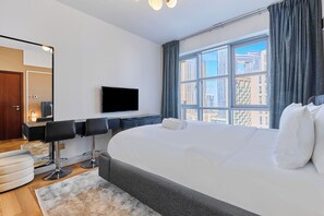 A modern hotel room with a large bed, a TV, a desk with chairs, and a view of the cityscape. - bnbme | Stand Point Tower A | 1BR + Study Room (Dubai)