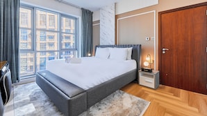 Een moderne slaapkamer met een groot bed, een nachtkastje, een houten garderobe en uitzicht op gebouwen door een groot raam.
