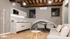 A modern kitchen with a built-in oven, a dining area with a round table and chairs, and a grey sofa with cushions. - [Maison Fontebella 56] Assisi Center (Assisi)