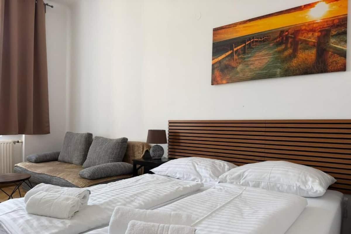 A hotel room with a bed, a chair, a nightstand, and a painting on the wall.