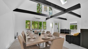 Un comedor moderno con una mesa larga dispuesta para seis personas, rodeada de sillas. Amplias ventanas proporcionan luz natural y vistas a zonas verdes.